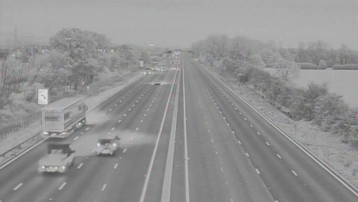 A black and white traffic camera image shows vehicles on one side of a road while all four lanes on the other side are empty
