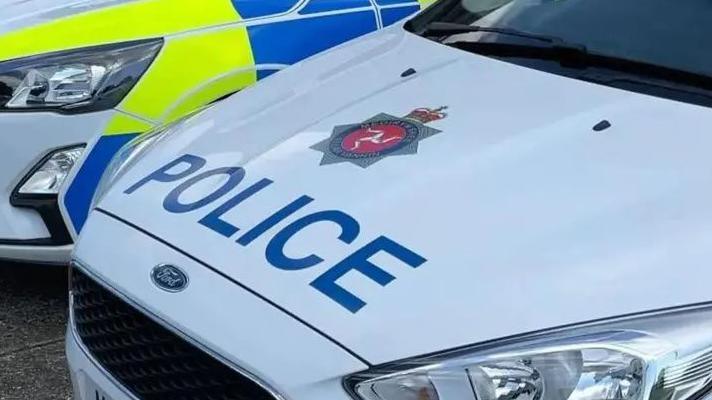 The bonnet of a white car which reads police in blue and has the three legs of man in a star which is the police logo.