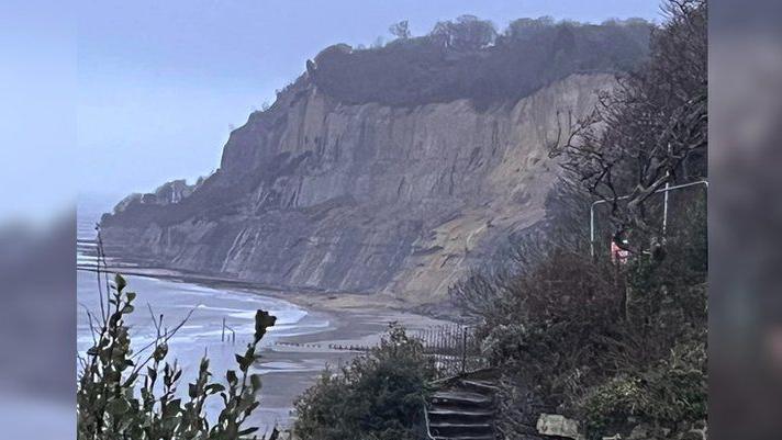 Luccombe Bay - a beach with grey cliffs. It looks like the tide is in. In the foreground, there are some steps.