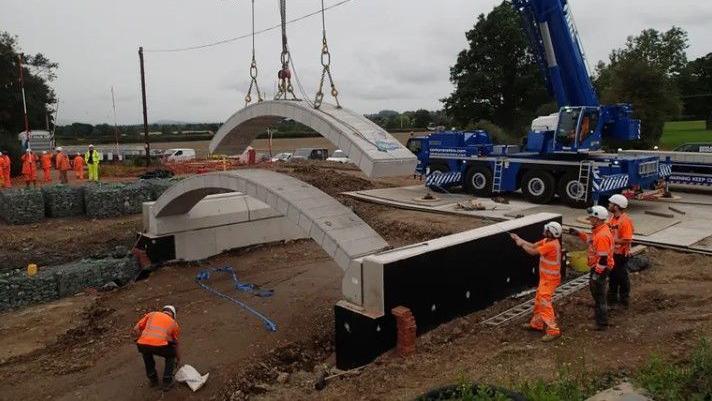 Construction workers lower bridge sections into place