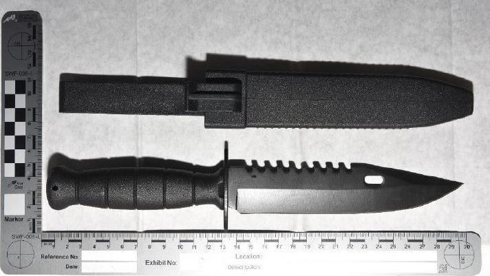 A knife with a black handle and a sharp point. It has a ridged edge on part of the blade. It is next to an evidence ruler.