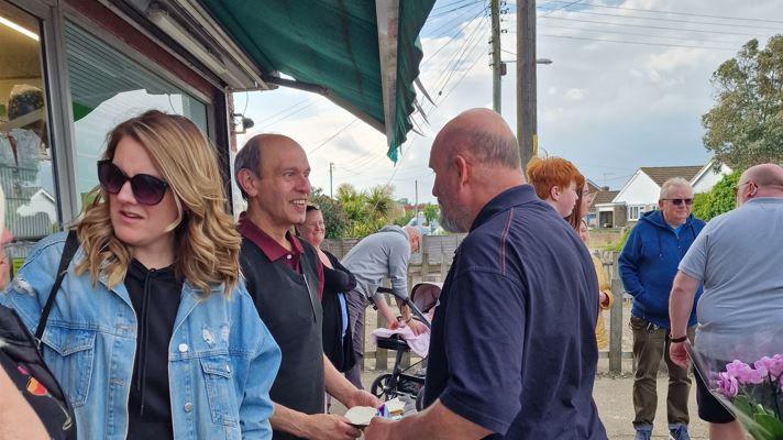 A group of people gathered outside a shop under a green awning and smiling