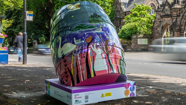 A multi-coloured barrel is tilted backwards on a base in a street.