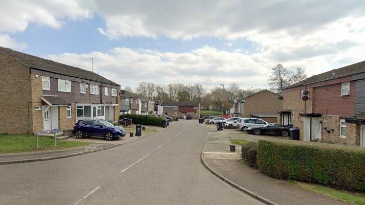 Residential housing estate street with two-storey brick houses with cars in most of the drives. A street sign says "Nethermead Court".