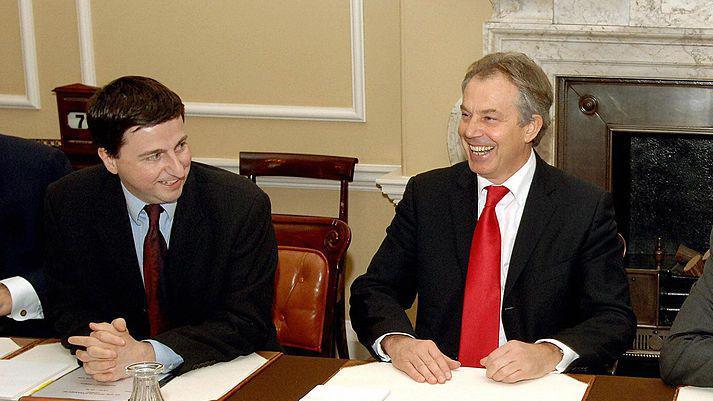 A picture from 2006 of Douglas Alexander (a youngish fellow with dark hair in a dark suit) sitting at the cabinet table with Tony Blair (a middle-aged man at the time, with lighter hair and a bright red tie) - both are laughing and smiling.