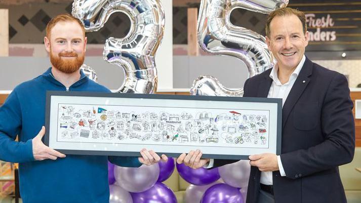 Luke Horton (left) holds a small version of the mural he was commissioned to create on the wall near Oasis food court