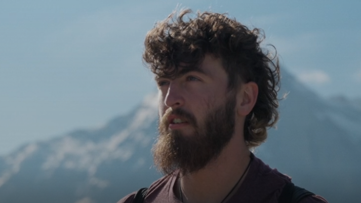 Man with beard looking out to the horizon at top of a mountain