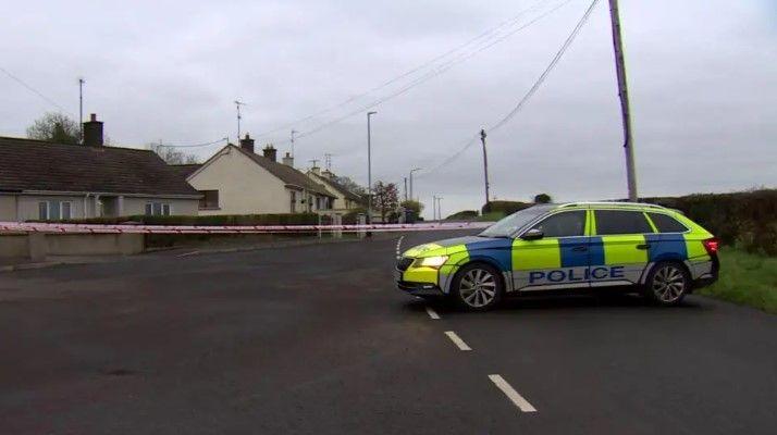 A police car is seen parked in the middle of a road with a number of houses to one side. A police cordon is in place. 