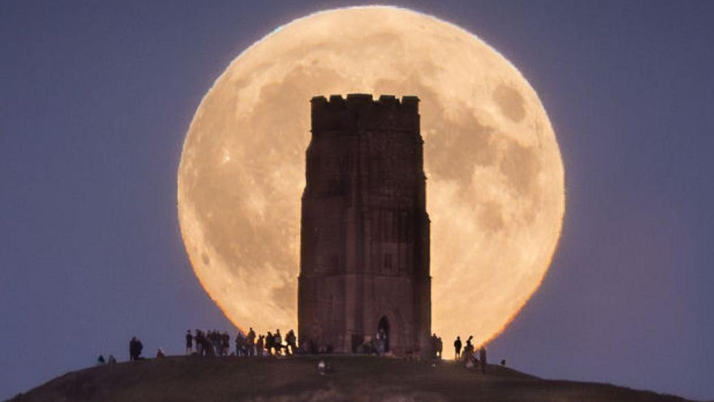 Visitors surrounding Glastonbury Tor at night with the huge Hunter's Moon visible behind with a golden glow