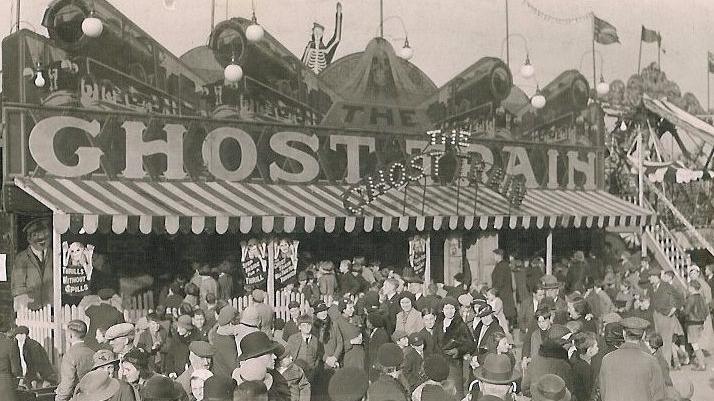 A black and white image of a ghost train ride with people standing around outside