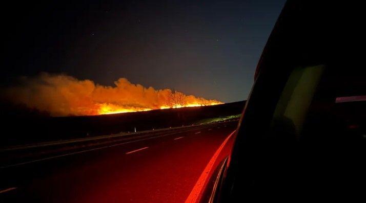 A wildfire at night. Smoke is rising into the sky. The photo has been taken from a car.