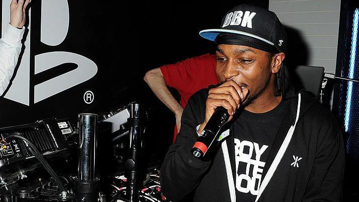 JME, wearing a black cap with "BBK" written on it, rapping into a microphone in a studio