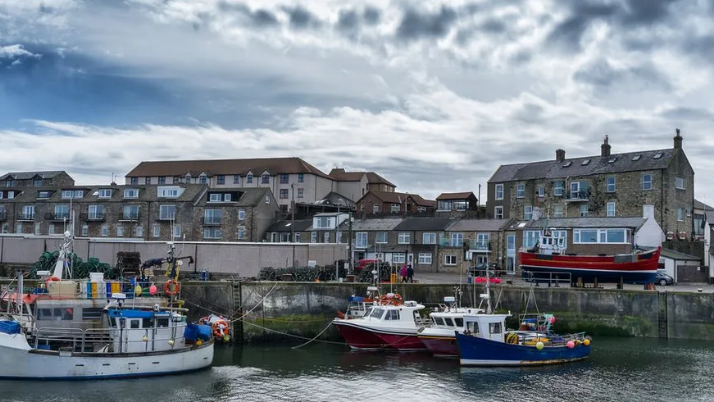 A picture of the harbour at Seahouses with boats moored up and rows of houses behind 