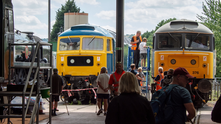 A railway works shed with two locomotives and people milling around