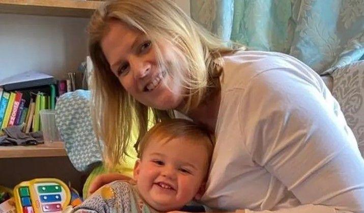 Julia is sitting with her son Louis in her lap. They are on a sofa and books and toys are shown in the background.