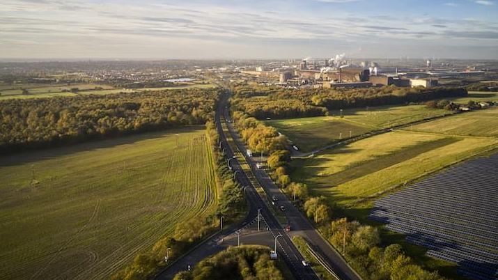 Aerial view of Mortal Ash Hill with trees along the side of the road and the town's steelworks in the distance.