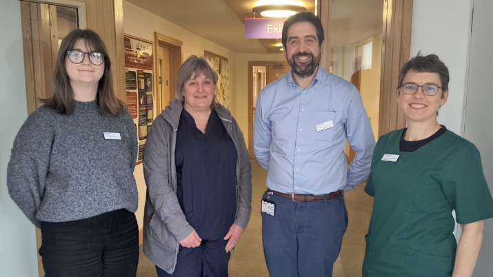 The photo shows the research team at ReMind UK.  The three women and a man are standing in a corridor and are smiling into the camera.