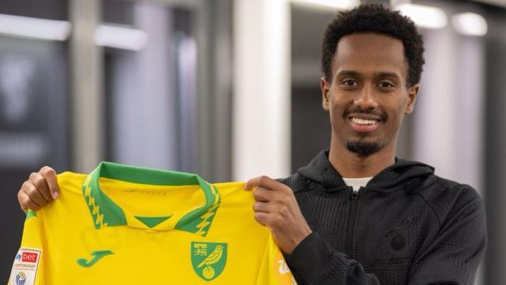 Ali Ahmed holding a yellow Norwich City shirt