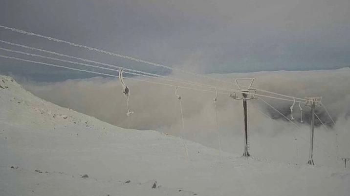 Ski tows and cables are covered in ice and there is a covering of snow below. Cloud obscures mountains in the background.