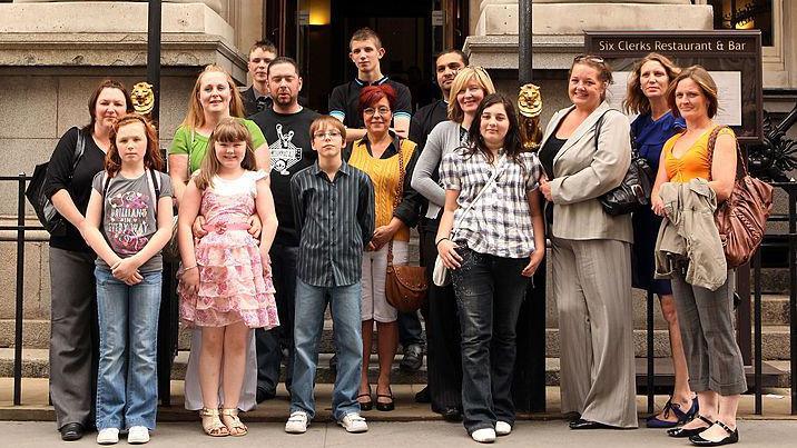 A group of families standing in front of a building with a black fence behind them. Some of them are smiling.