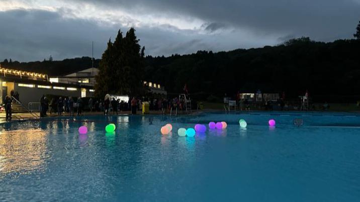 Light -up multicoloured inflatable balls on the lido water at dusk