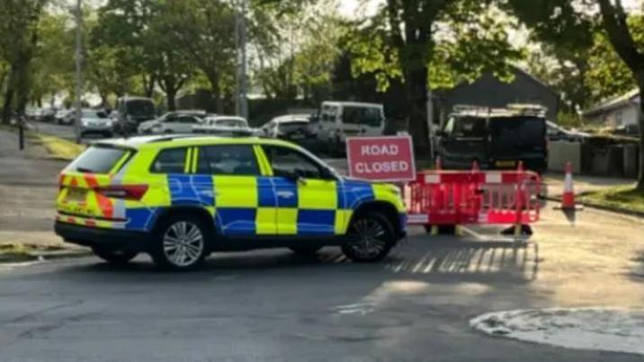 A police car sits ahead of a road closed sign on the road