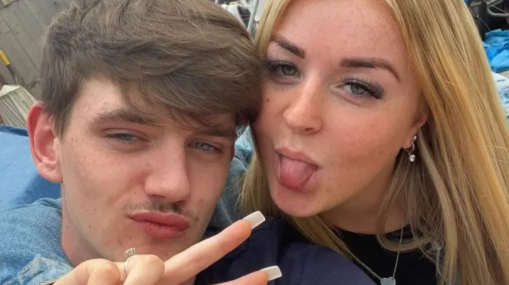 Tyler Kerry, who has brown hair swept across his head and is pouting. A woman with blonde hair has her arm around him and is doing a peace sign with her fingers while sticking her tongue out.