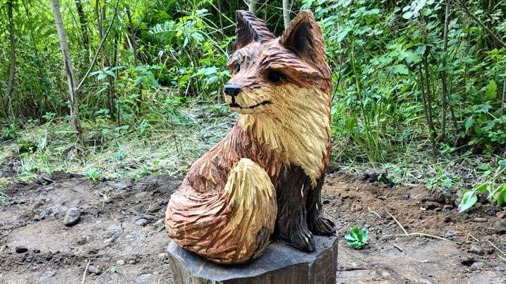 A wooden sculpture of a brown fox sitting upon a log