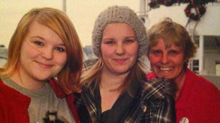 A group of three women in a smiling, happy family photo. They are a middle aged mum and her two teenage daughters.