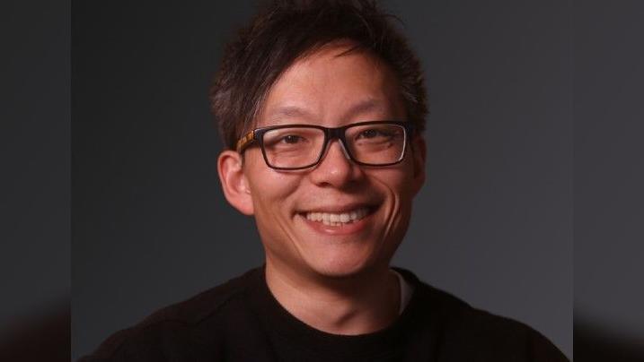 James Lim wearing a black t shirt and glasses while smiling at the camera. It is a professional photo.