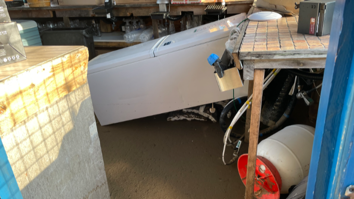 A fridge tipped over behind a bar with mud on the floor