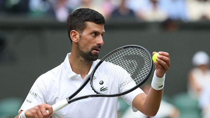 Novak Djokovic holding a tennis ball and tennis racket.