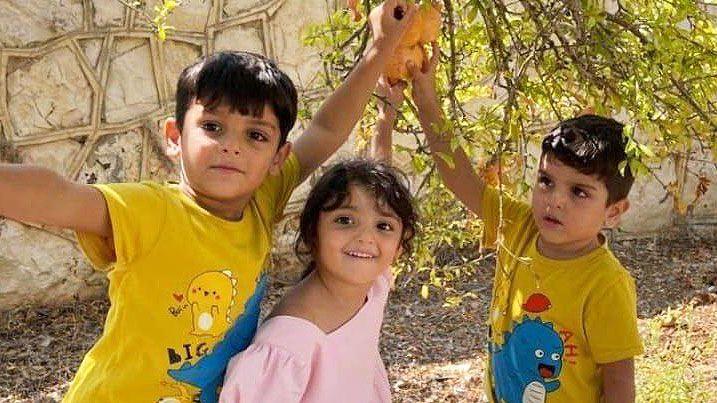 Hawraa, and her cousins Hassan and Hussein, photographed playing together. Hawraa is wearing a pink dress with puff sleeves and a square neck line. Her cousins are both in yellow cartoon dinosaur t-shirts.