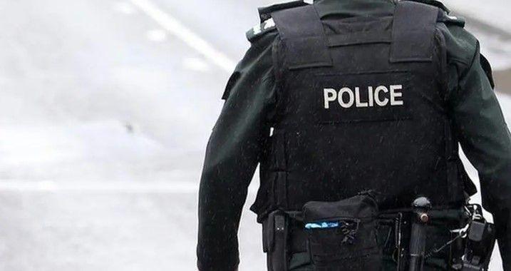 A police officer is standing on a road. They are in a black uniform and have a belt with a number of items.