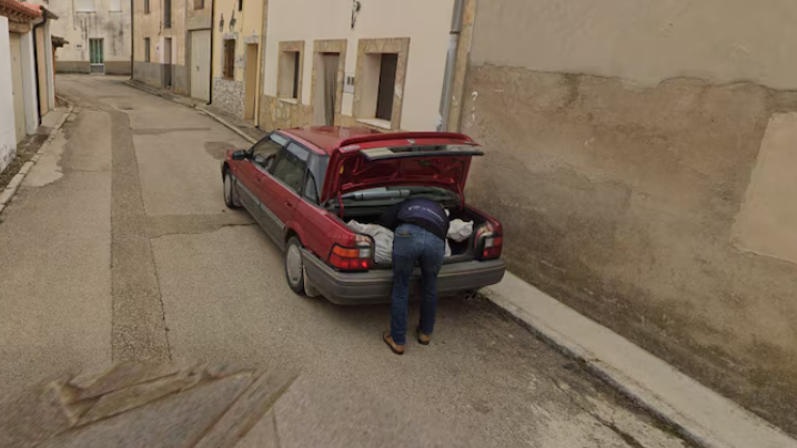 A Google Streetview image of a man bending over the boot of a car loading in a body