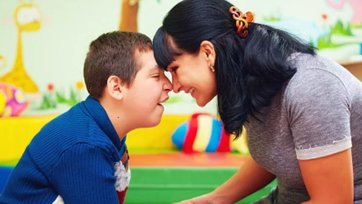 A boy in a blue shirt touches noses with a woman