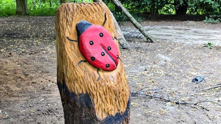 A wooden sculpture of a red ladybird on a tree.