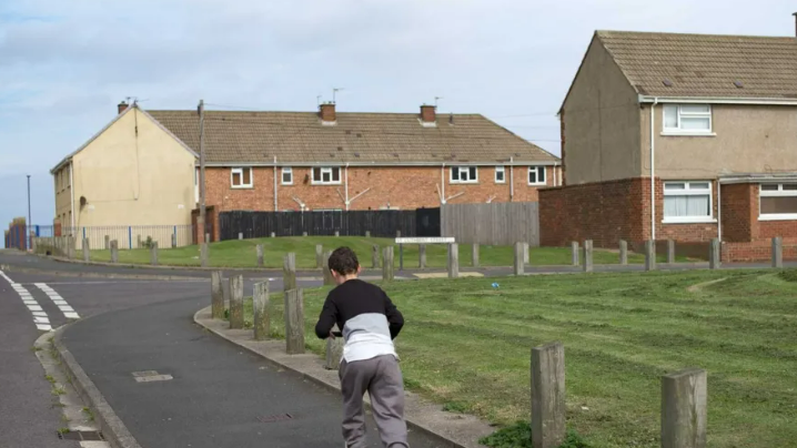 A child on a scooter rides on the pavement towards a council estate.