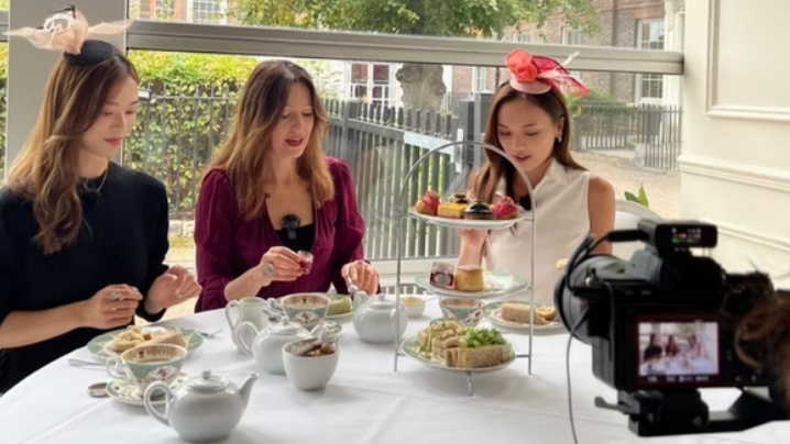 Laura Windsor sits down for afternoon tea with two other women. They are eating sandwiches and drinking tea, and are dressed formally.