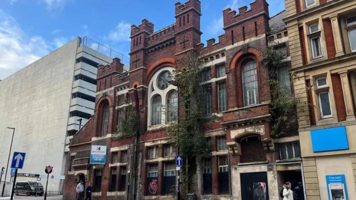 A red building with turret-like bricks at the top of the facade and glass windows in the middle of the building.