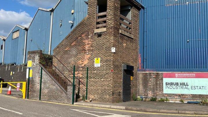 An industrial building, with blue corrugated sheeting and brick-built sections. There is a sign with the words Shrub Hill Industrial Estate in capital lettering.