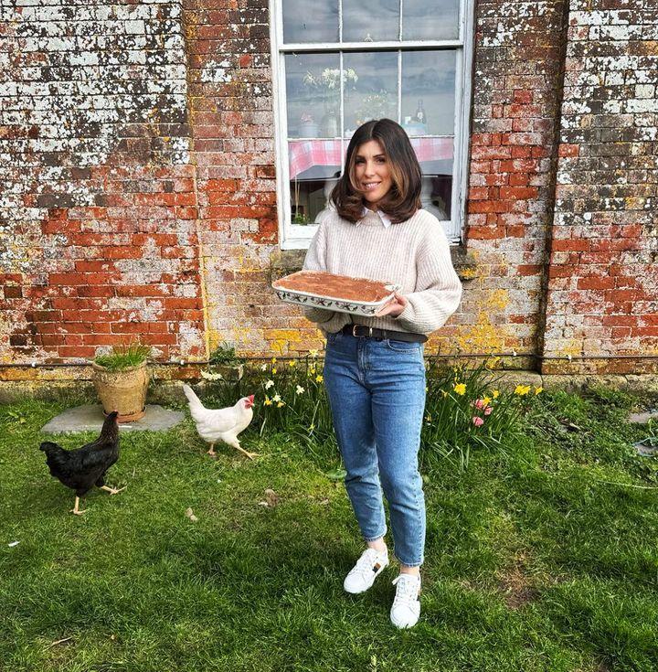 A woman holding a tray of baked goods in front of a rural building.