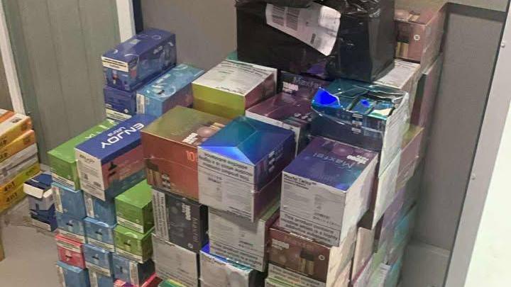 About 30-40 different coloured cardboard boxes storing illegal vapes stacked one on top of the other in a storage unit. Different vape brand names are on the boxes.