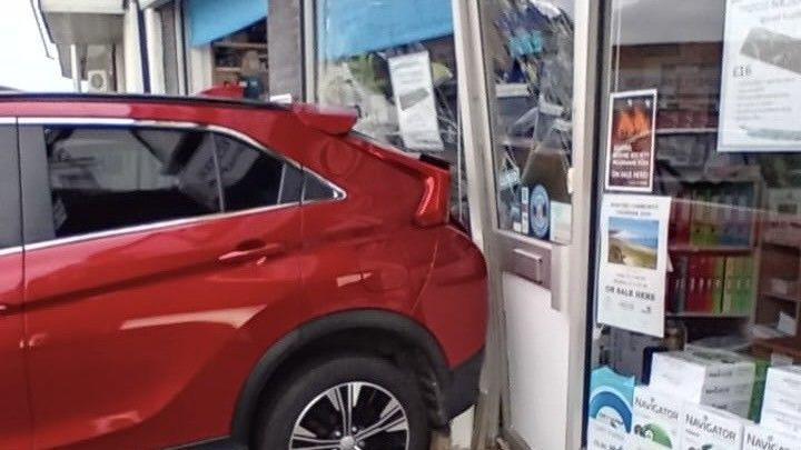 The glass front of a shop is smashed by a red car