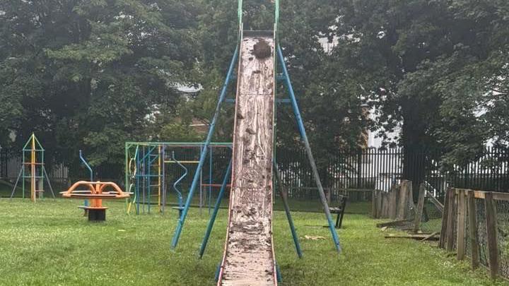 Mud smeared all over a slide in Wigton park. The slide is located next to a damaged fence, which has some of its panels missing.