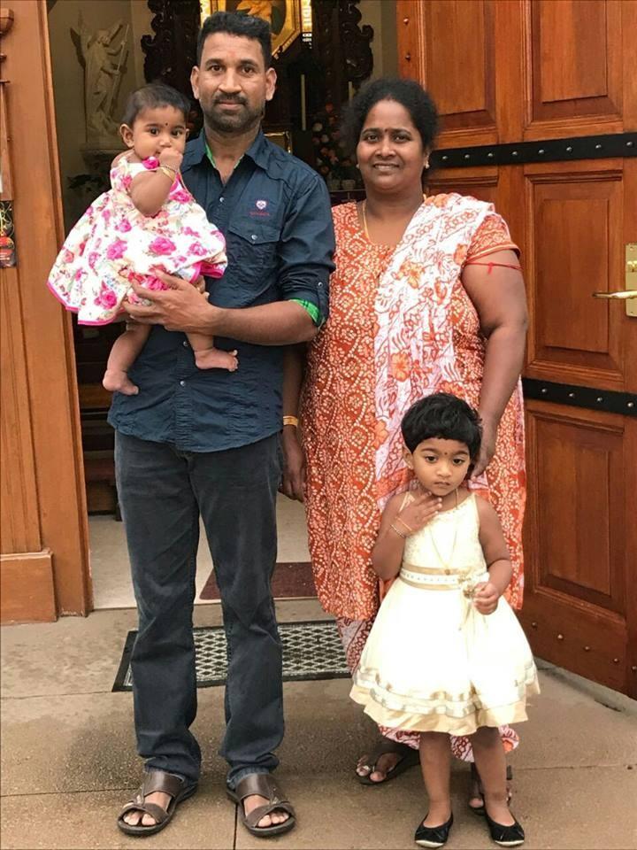 A family picture of Nadesalingam and Priya and their two daughters outside a door.