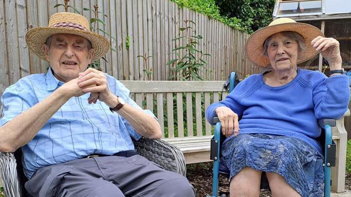 Peter and Eileen sit outside with straw sun hats on.