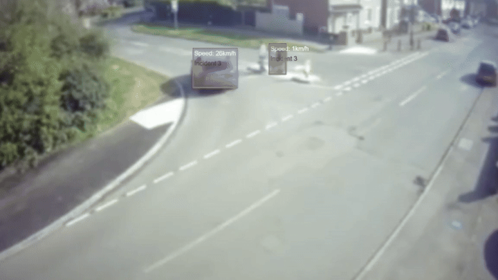 A vehicle is seen turning into the road with pedestrians standing safely in an area in the middle of the road.