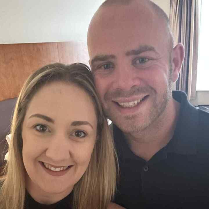 A smiling woman with long blonde hair is photographed with a smiling man with stubble.