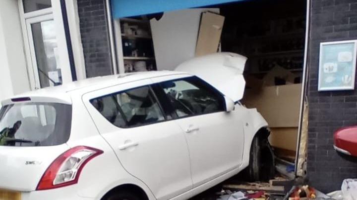 A white car has smashed through the front of a shop.